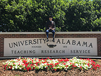 Justin Murphy sitting on a University of Alabama sign