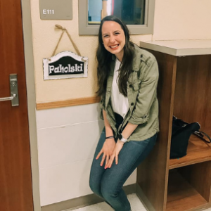 Becca in front of her classroom with "Paholski" as a the sign next to the door