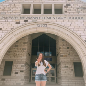Becca holding up four fingers in front of her school, Newman Elementary
