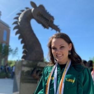 Emma in her UAB graduation robes standing in front of a dragon statue at UAB