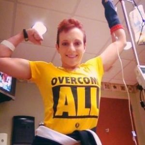 Kristen in the hospital flexing her bicep with an "Overcome All" shirt on