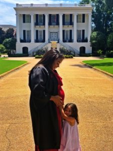 Franky with her daughter in front of the UA president's mansion on the day she graduated with her bachelor's. In the photo, she is looking down at her pregnant belly through her graduation robe opening, and her daughter is hugging her belly.